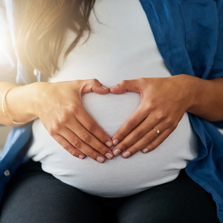 Der Bauch einer Schwangeren wird von Händen umfasst.